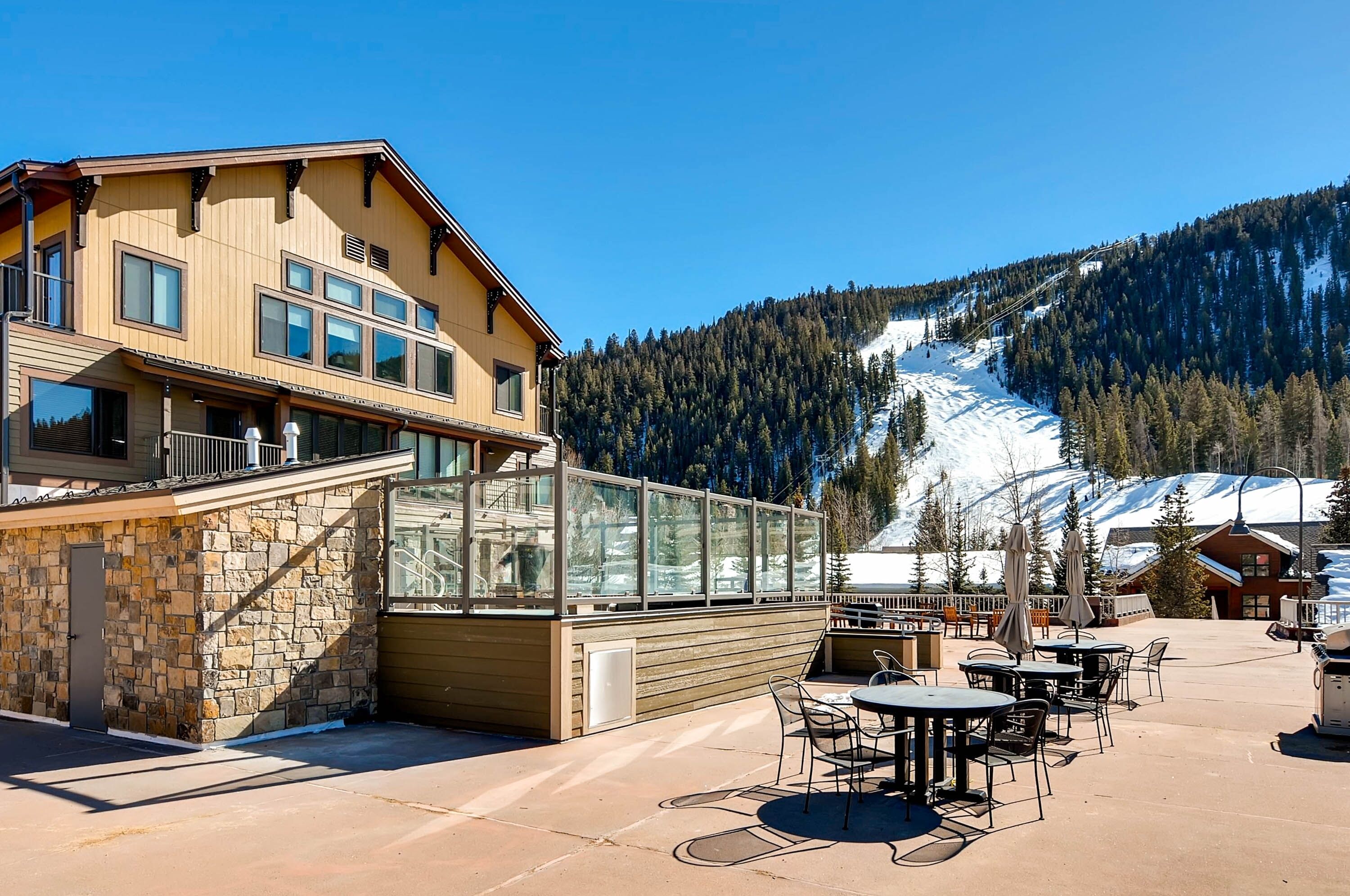 A building with a stone facade and a glass enclosure, outdoor seating area, and a view of a snowy mountain.