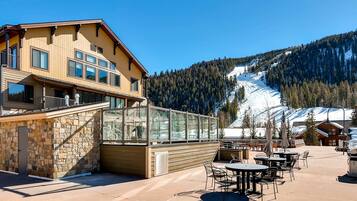 A building with a stone facade and a glass enclosure, outdoor seating area, and a view of a snowy mountain.