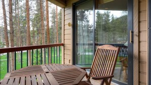 Eine Holzdielen-Terrasse mit Tisch und Stuhl, mit Blick auf ein bewaldetes Gebiet.