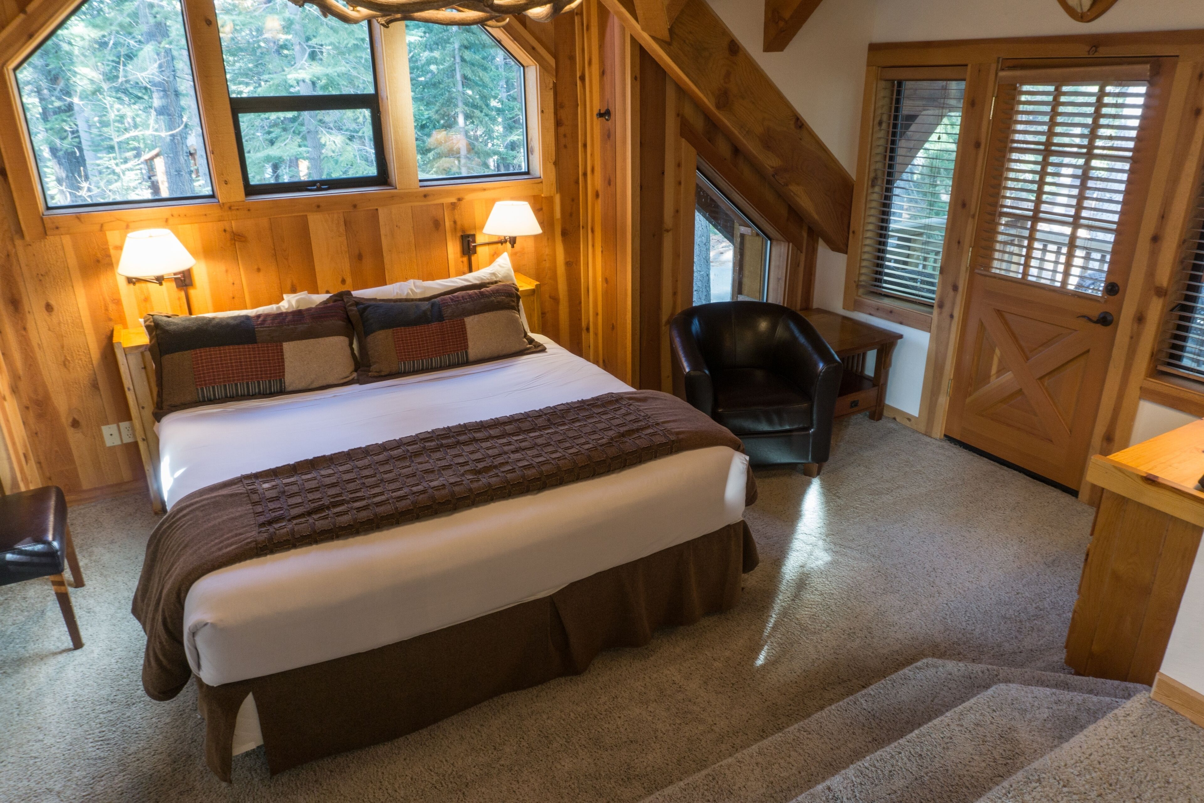 A bedroom with a large bed, two bedside lamps, a chair, and a door with a window.