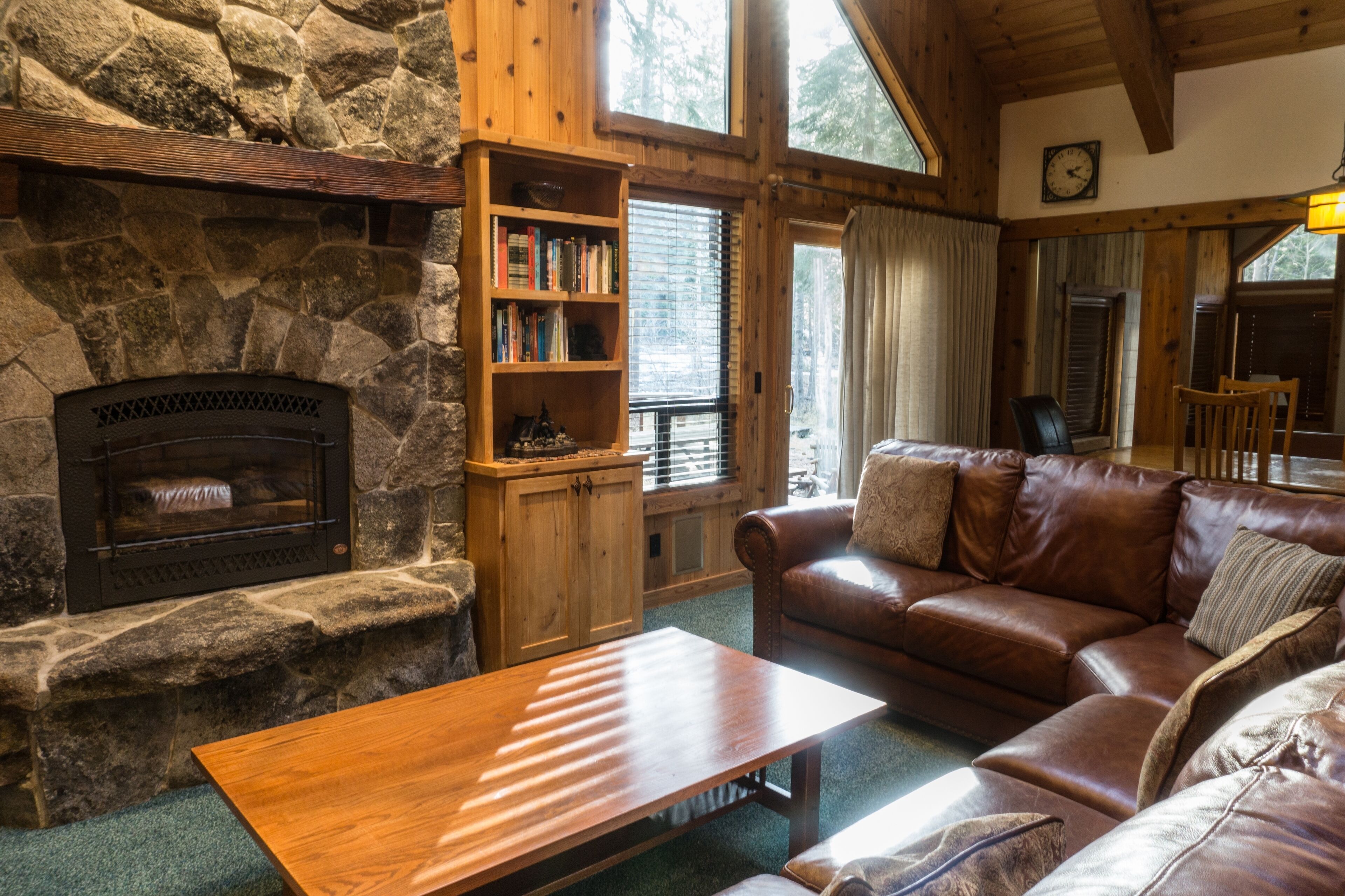 A cozy living room with a stone fireplace, a wooden bookshelf, a leather sofa, and a wooden coffee table.