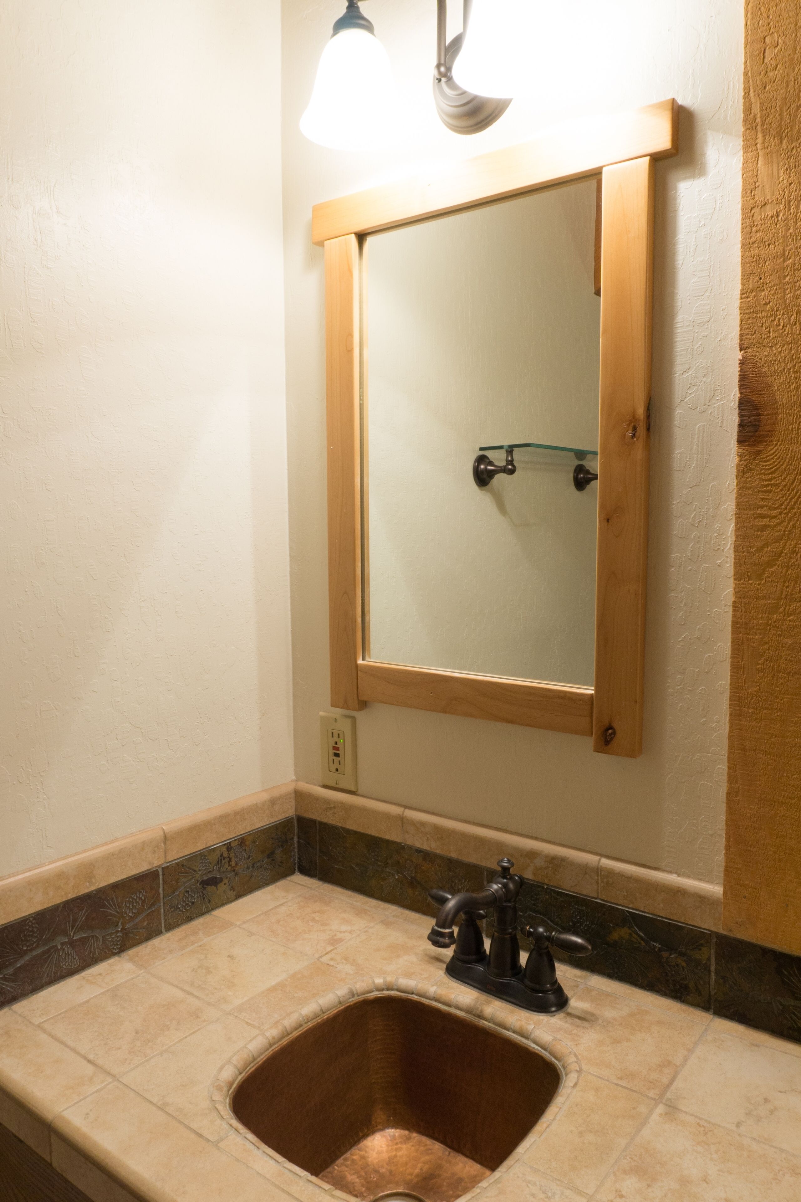 A bathroom with a wooden-framed mirror, a sink with a faucet, and a light fixture above the mirror.