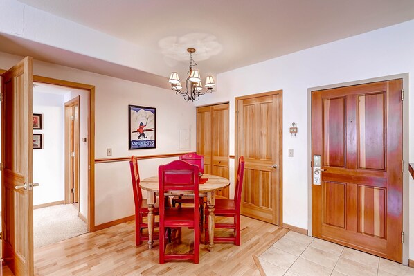 A dining area with a wooden table and red chairs, a chandelier, wooden doors, and a framed picture on the wall.