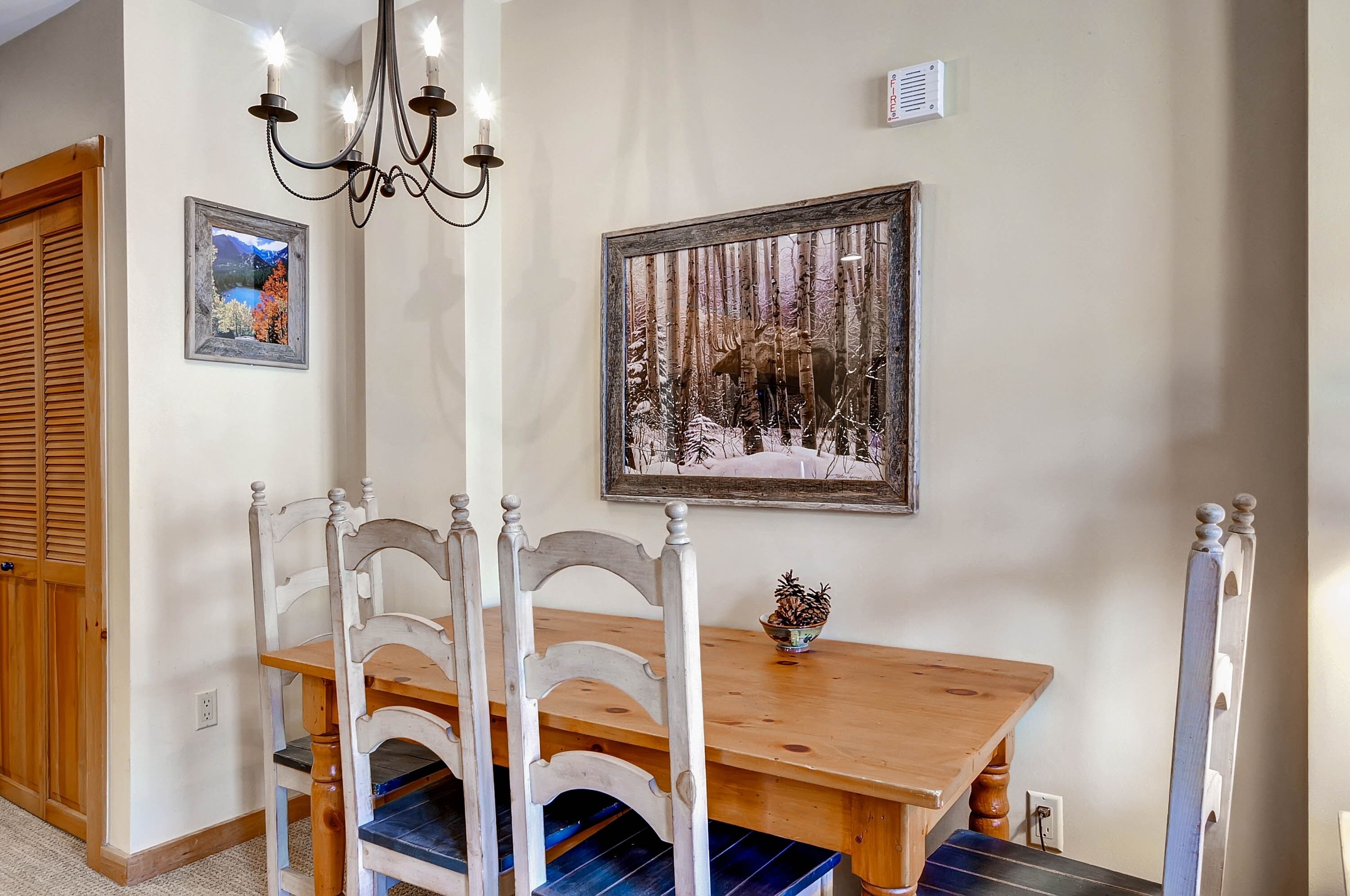 A dining area with a wooden table and chairs, a chandelier, and two framed pictures on the wall.
