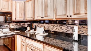 A kitchen with wooden cabinets, a black countertop, a stove, and a coffee maker. - Spacious, Upgraded 2 Bdr W/ Fireplace & Hot Tub Access 2 Bedroom Condo by RedAwning (Keystone)