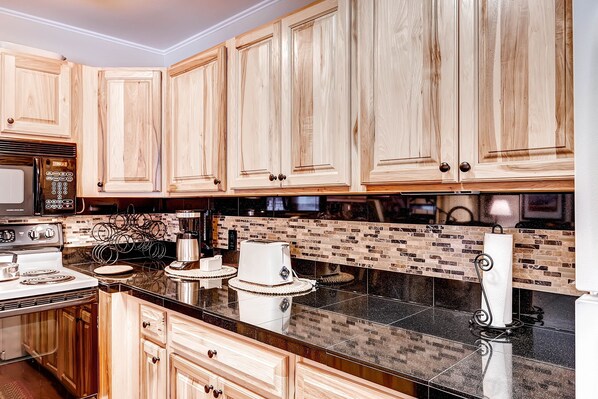 A kitchen with wooden cabinets, a black countertop, a stove, and a coffee maker.