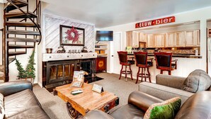 A living room with a fireplace, a wooden coffee table, leather sofas, and a staircase. - Spacious, Upgraded 2 Bdr W/ Fireplace & Hot Tub Access 2 Bedroom Condo by RedAwning (Keystone)