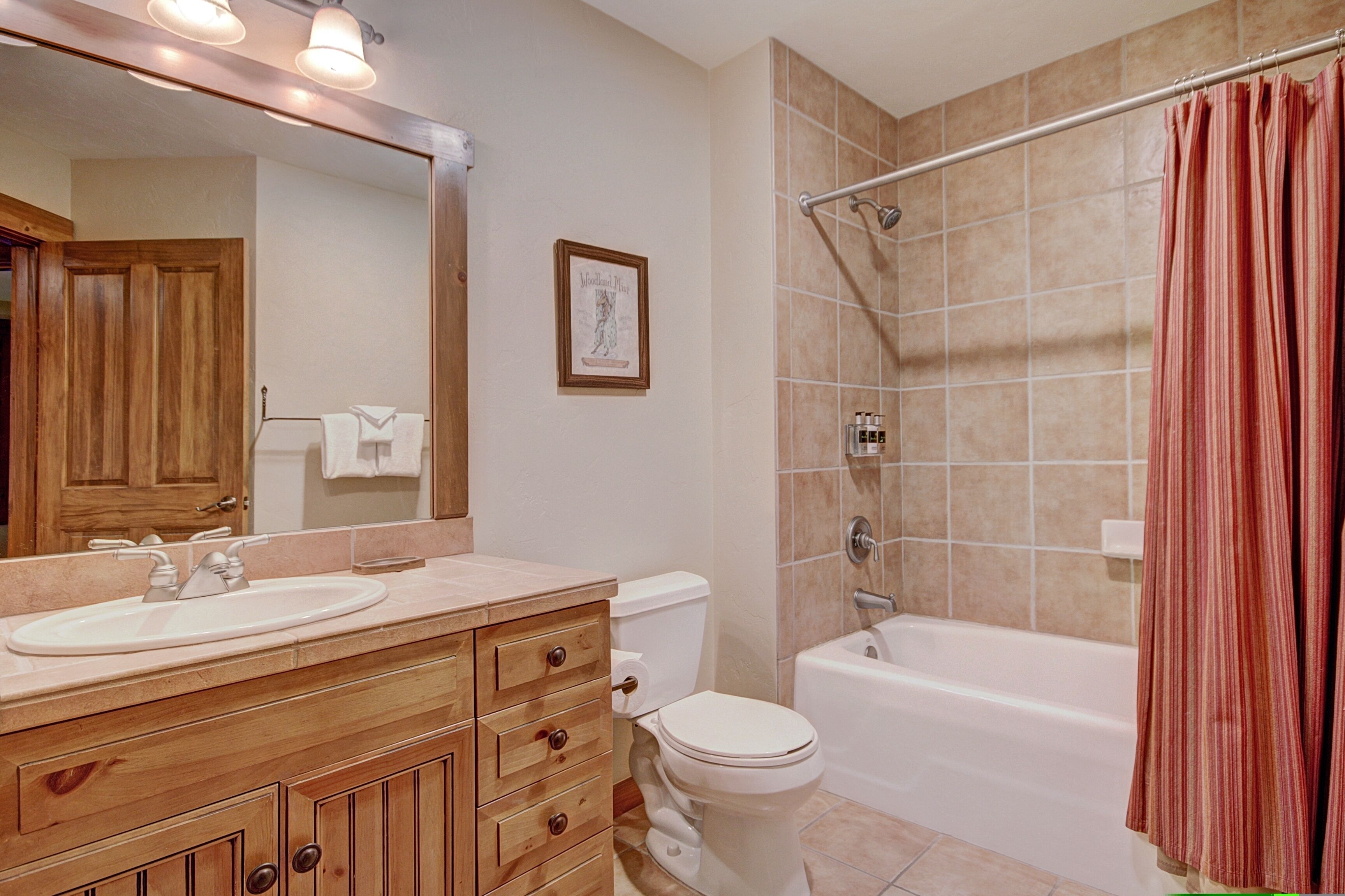 A bathroom with a wooden vanity, a white sink, a toilet, and a bathtub with a shower curtain.