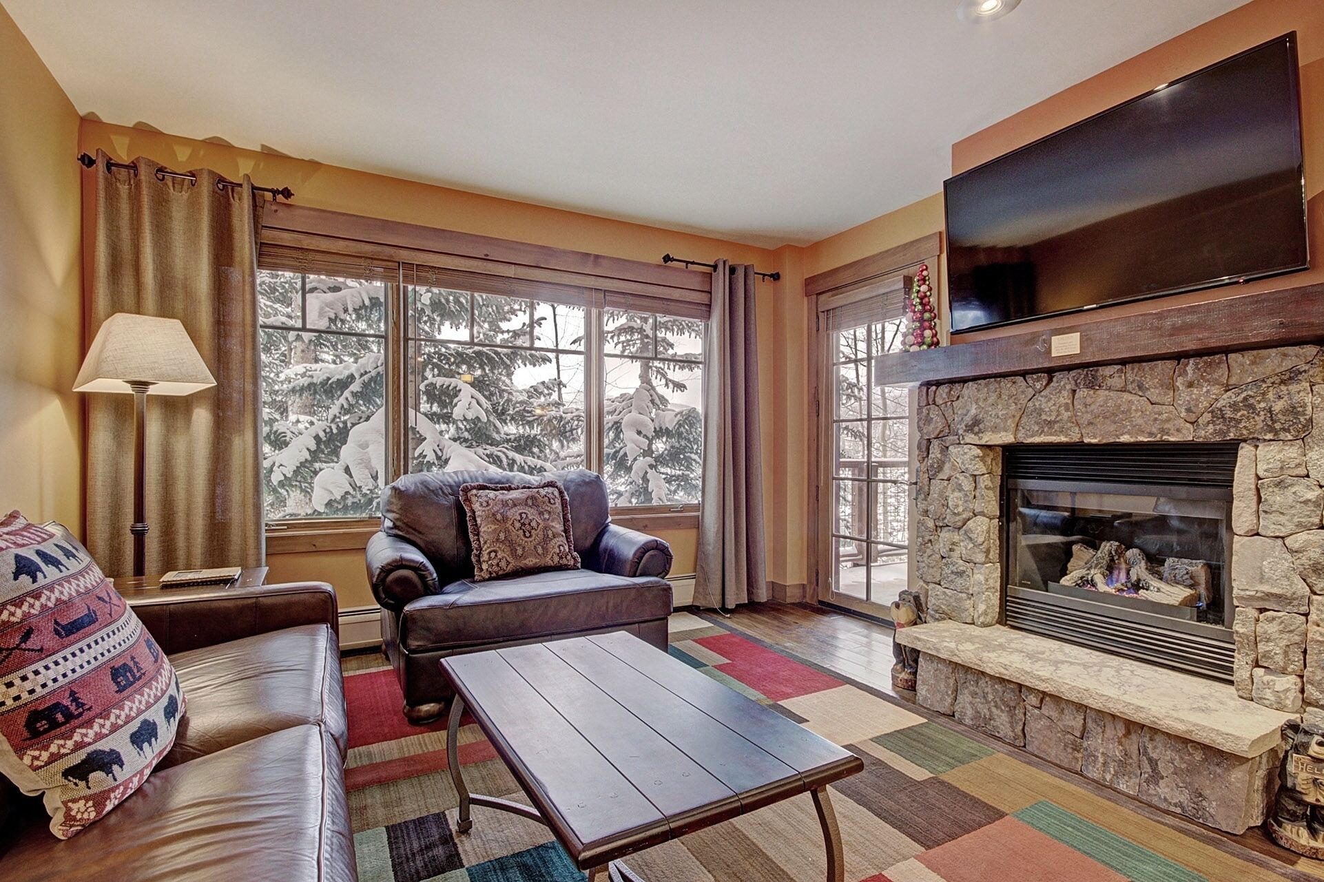 A cozy living room with a fireplace, leather sofa, and a television mounted above it.
