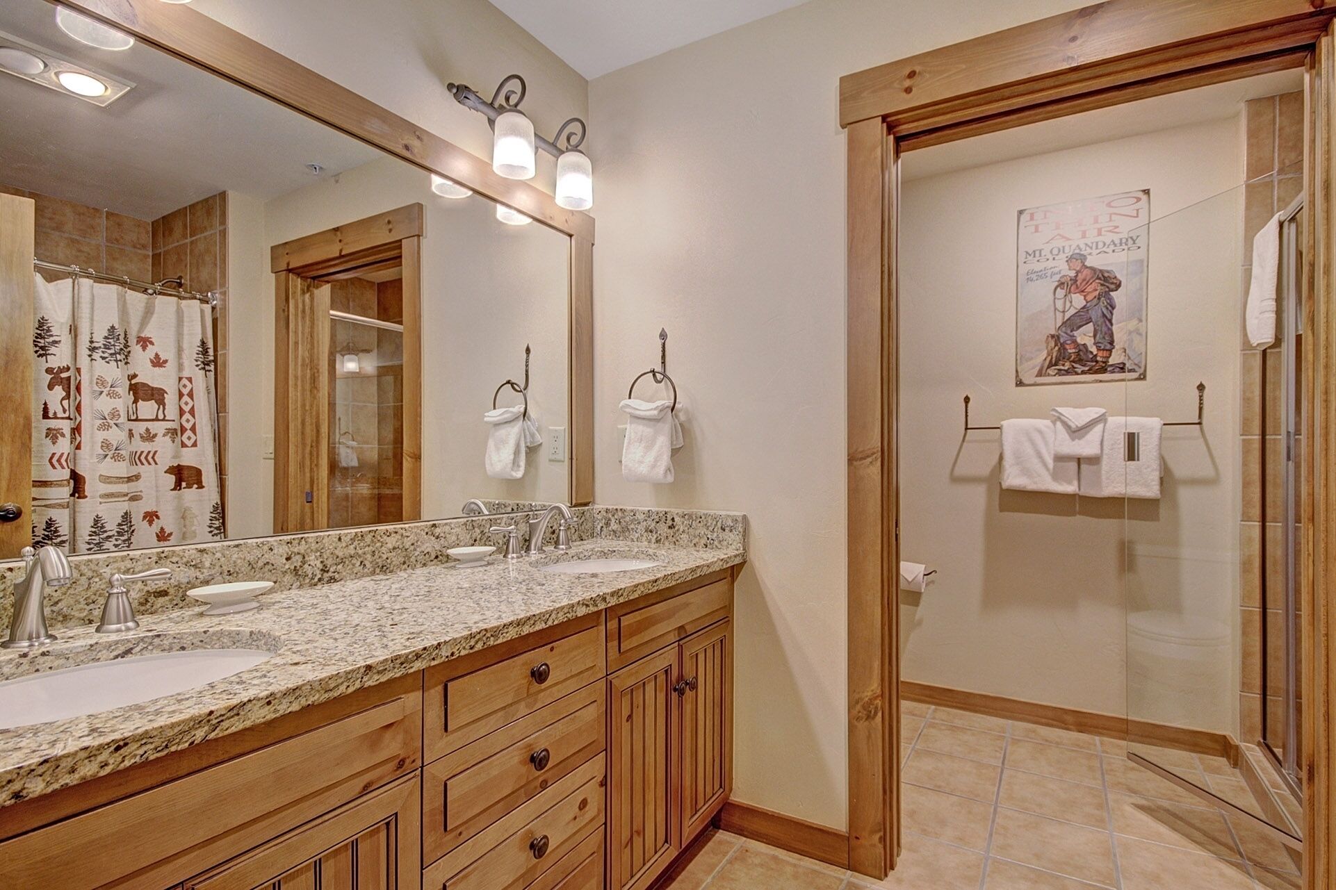 Un baño con encimera de granito, armarios de madera, un espejo grande y una ducha con puerta de vidrio.