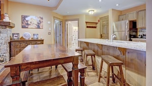 A modern kitchen with a wooden dining table, bar stools, and a built-in island with a sink. - Luxe 2br 2ba - Rocky Mountain Views + Walk To Mainstreet 2 Bedroom Apts by RedAwning (Breckenridge)