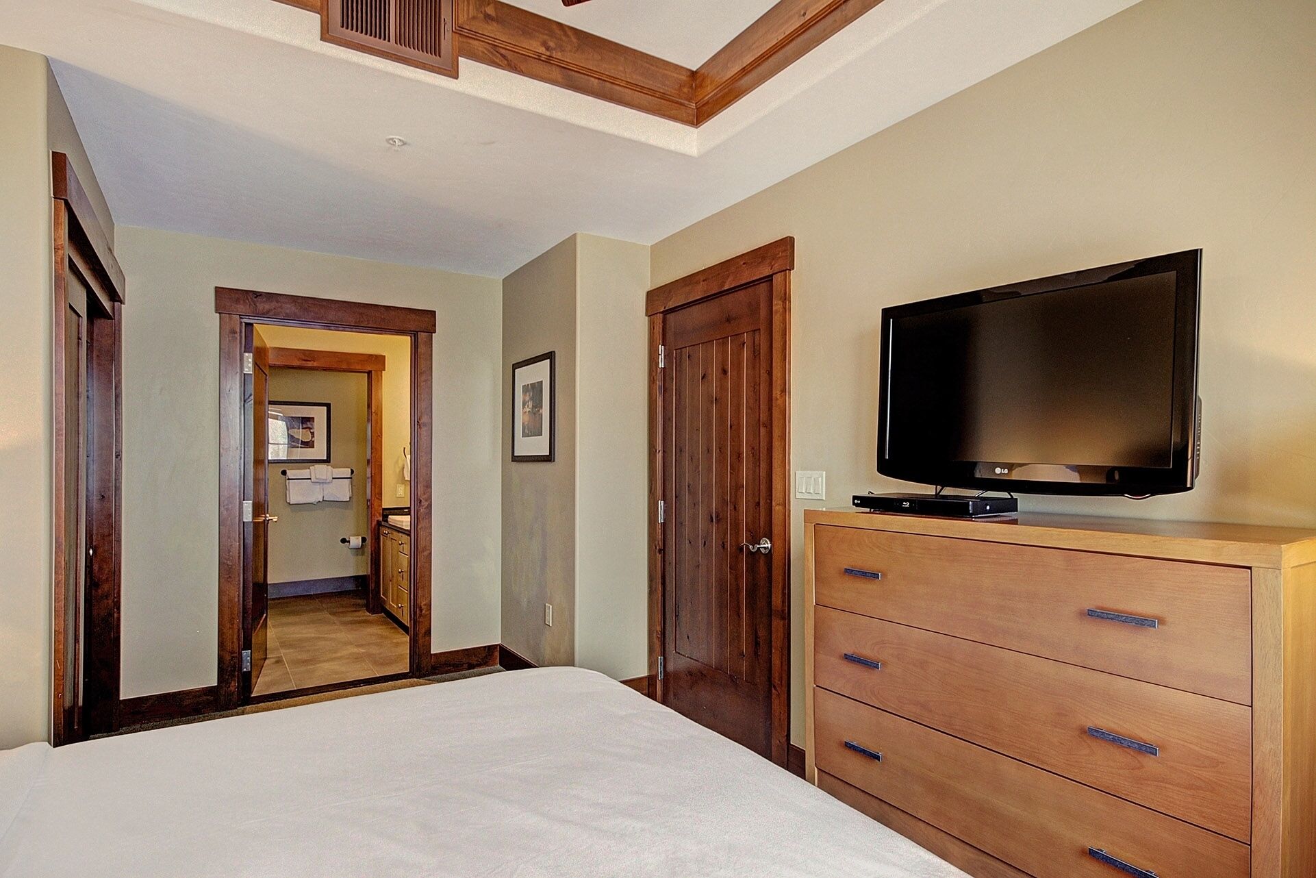 Un dormitorio con cama, cómoda de madera, televisión y una puerta que da a un baño.