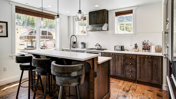 Una cocina moderna con una isla central, taburetes de bar, armarios de madera y ventanas amplias.