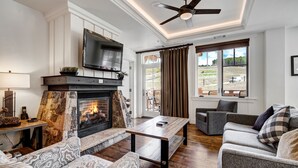 Una sala de estar con chimenea, un televisor de pantalla plana montado encima y un ventilador de techo.