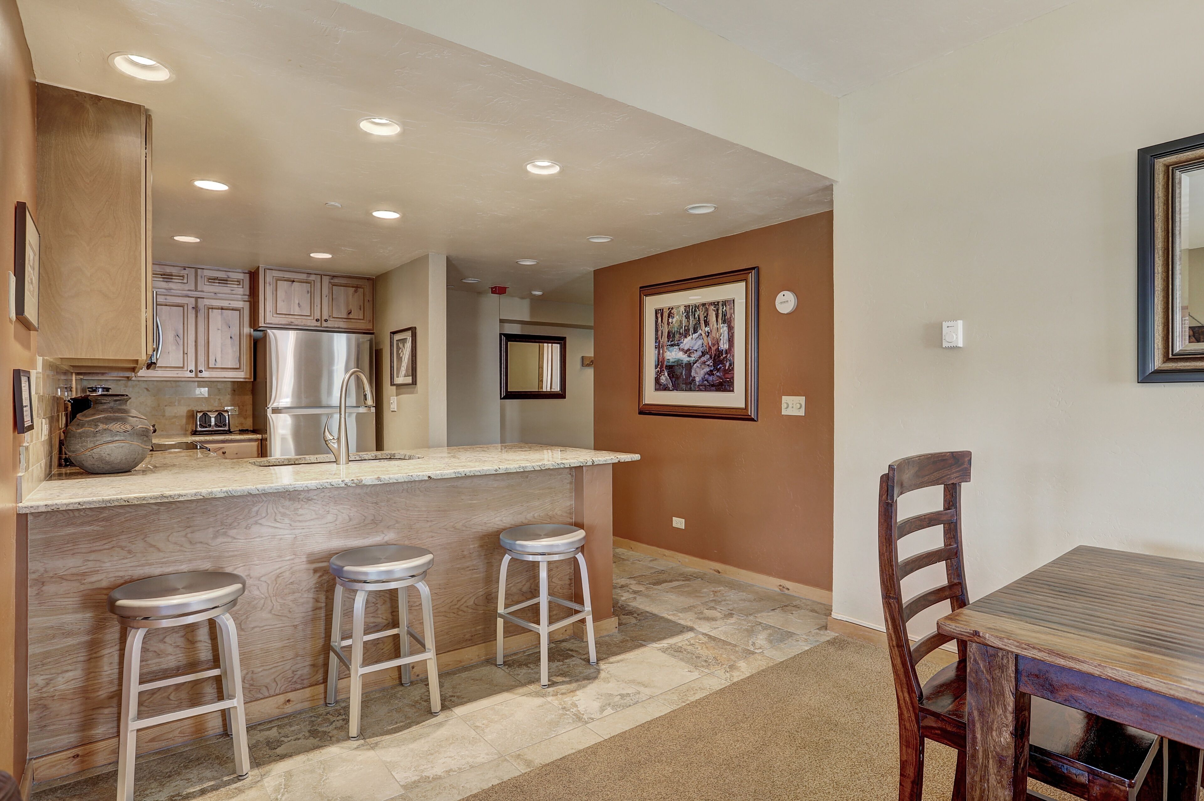 A modern kitchen with a central island, bar stools, and a dining table with a chair.