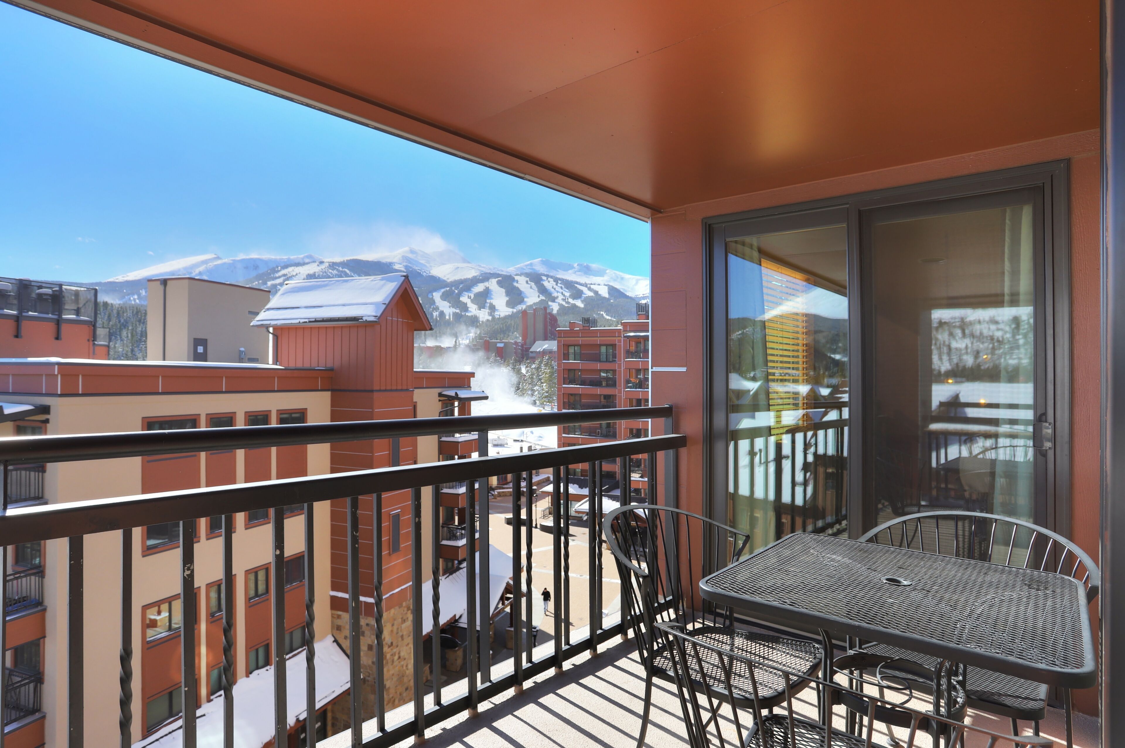 Een balkon met een tafel en stoelen, met uitzicht op een besneeuwde berg en gebouwen.