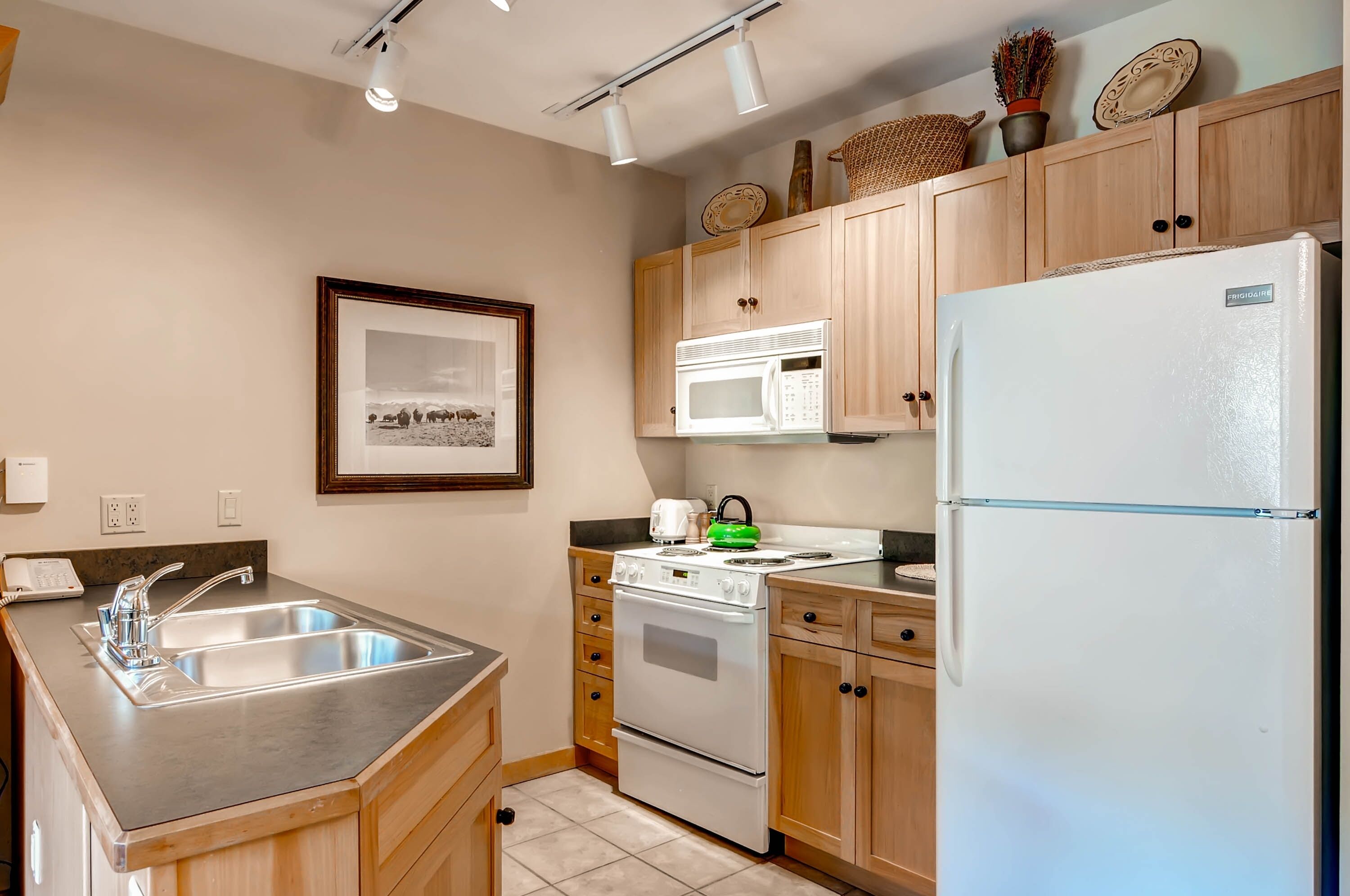 A kitchen with wooden cabinets, a stainless steel sink, a microwave, a stove, and a refrigerator.