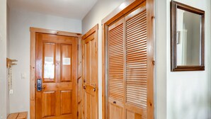 Una puerta de madera con manija y un ventanal pequeño, un banco de madera y un armario de madera con puertas persianas.