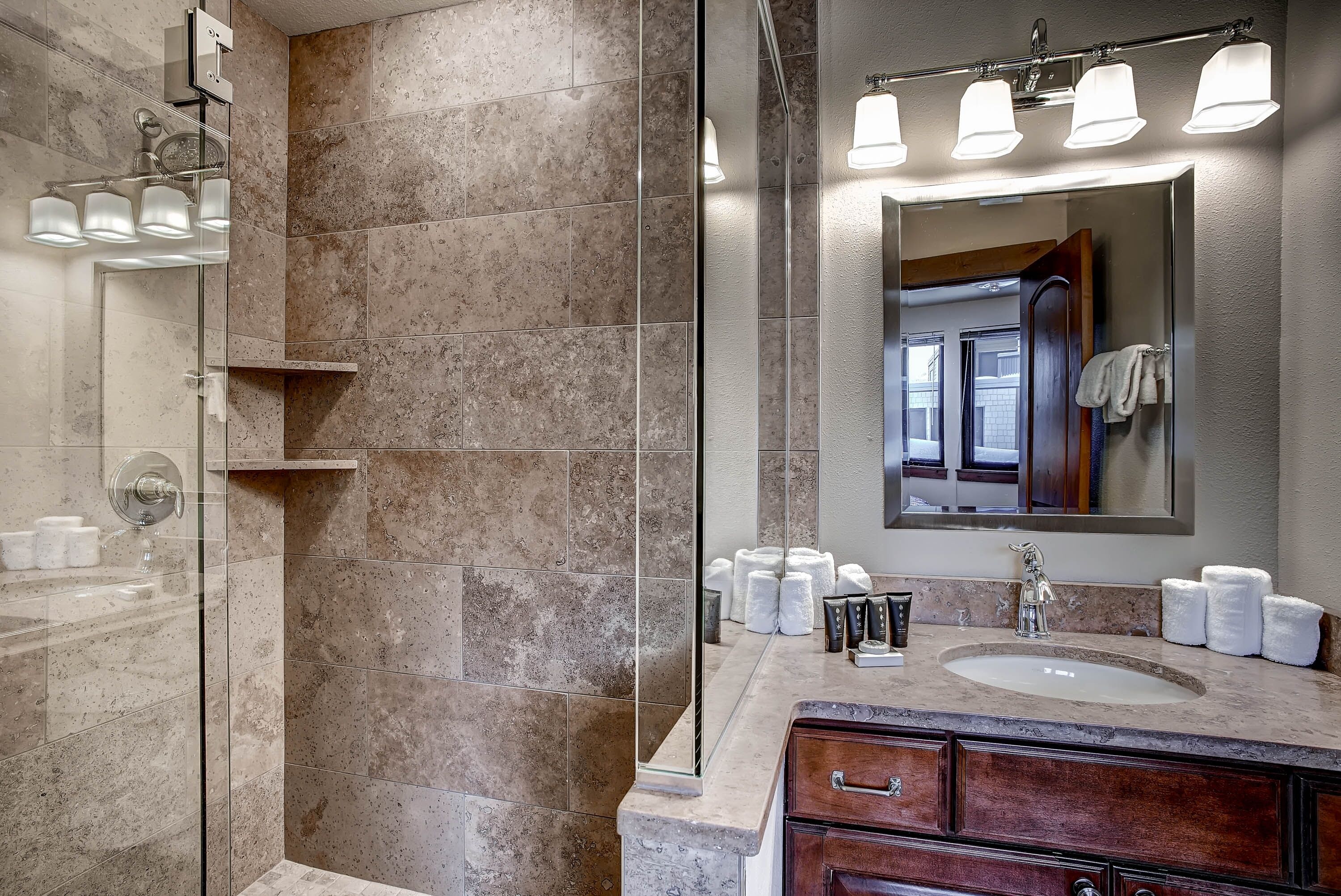 A modern bathroom with a glass-enclosed shower, a vanity with a sink, and a large mirror.
