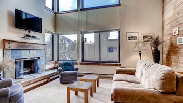 A modern living room with a fireplace, large windows, and a flat-screen TV.