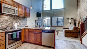 Una cocina moderna con armarios de madera, horno empotrado y lavavajillas. Hay un ventanal que proporciona luz natural y vistas al exterior.