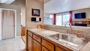 A modern kitchen with granite countertops, stainless steel sink, wooden cabinets, and a large window with a view. - Plaza 1407 (Keystone)