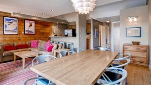 A modern living room with a wooden dining table, a sofa set, and a kitchen in the background. - Plaza 1407 (Keystone)
