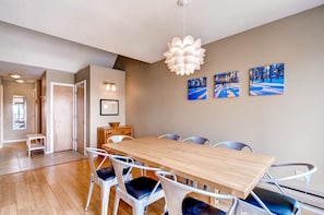 Een eethoek met een houten tafel en witte stoelen, een hanglamp en drie ingelijste foto's aan de muur.
