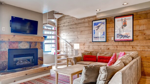 A modern living room with a fireplace, a sofa with red cushions, a TV mounted on the wall, and wooden paneling. - Plaza 1407 (Keystone)