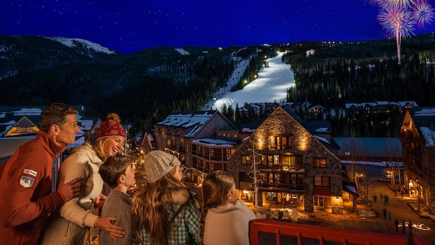 Un groupe de personnes s’est rassemblé dans un village enneigé, où les bâtiments étaient illuminés et où l’on pouvait apercevoir une piste de ski au loin.