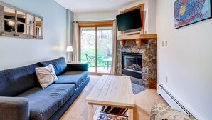 Un salon avec un canapé bleu, une table basse en bois, une cheminée et un téléviseur posé sur un meuble en bois.