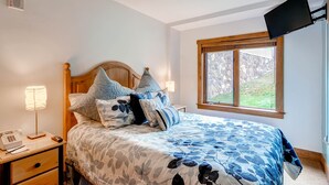 Une chambre à coucher avec un lit, des lampes de chevet, un téléphone et une fenêtre donnant sur un paysage verdoyant.