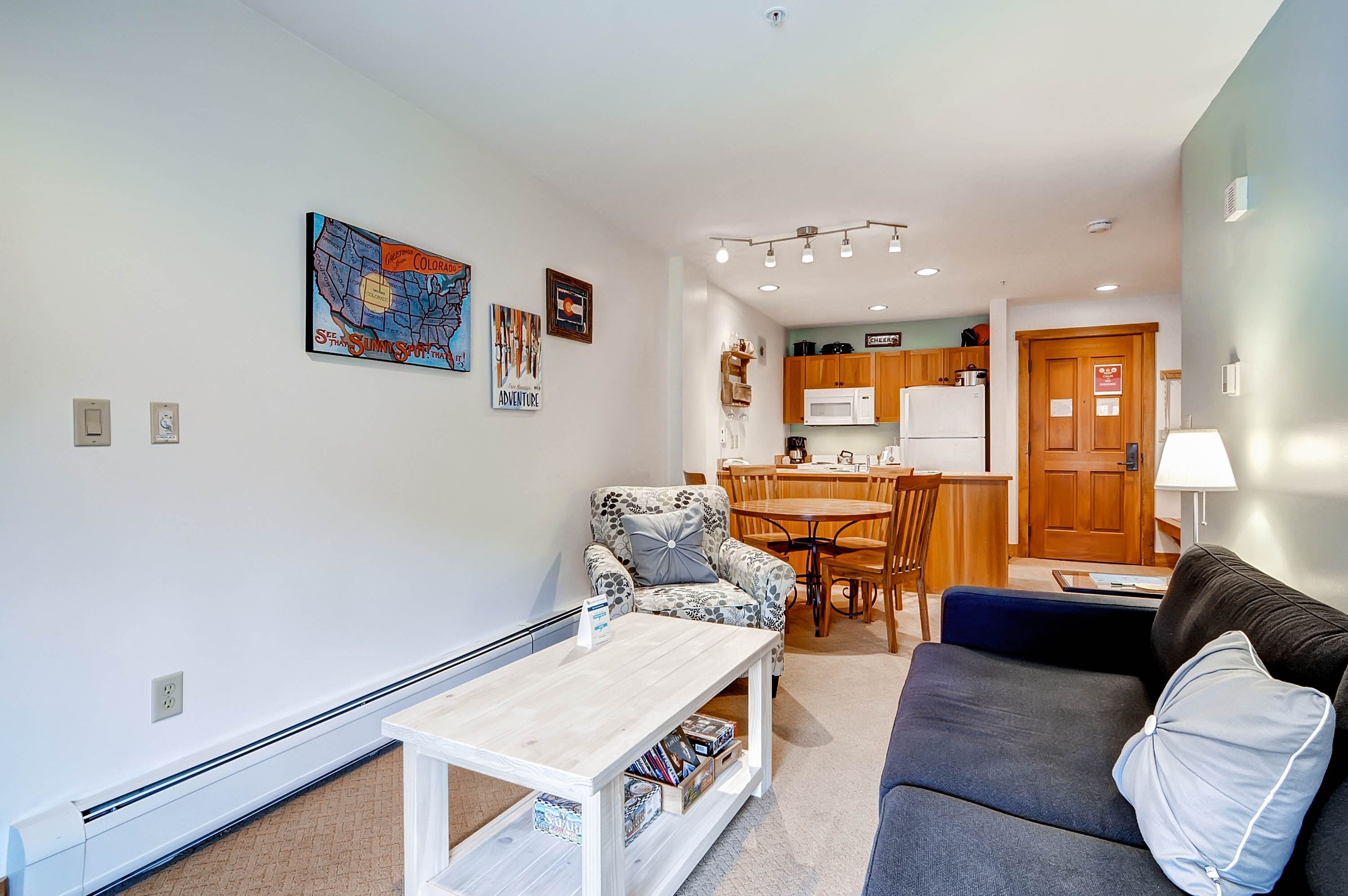 Een woonkamer met een bank, een gestreept fauteuil, een salontafel, en een eethoek met een tafel en stoelen.