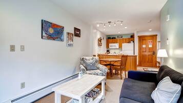 Een woonkamer met een bank, een gestreept fauteuil, een salontafel, en een eethoek met een tafel en stoelen.