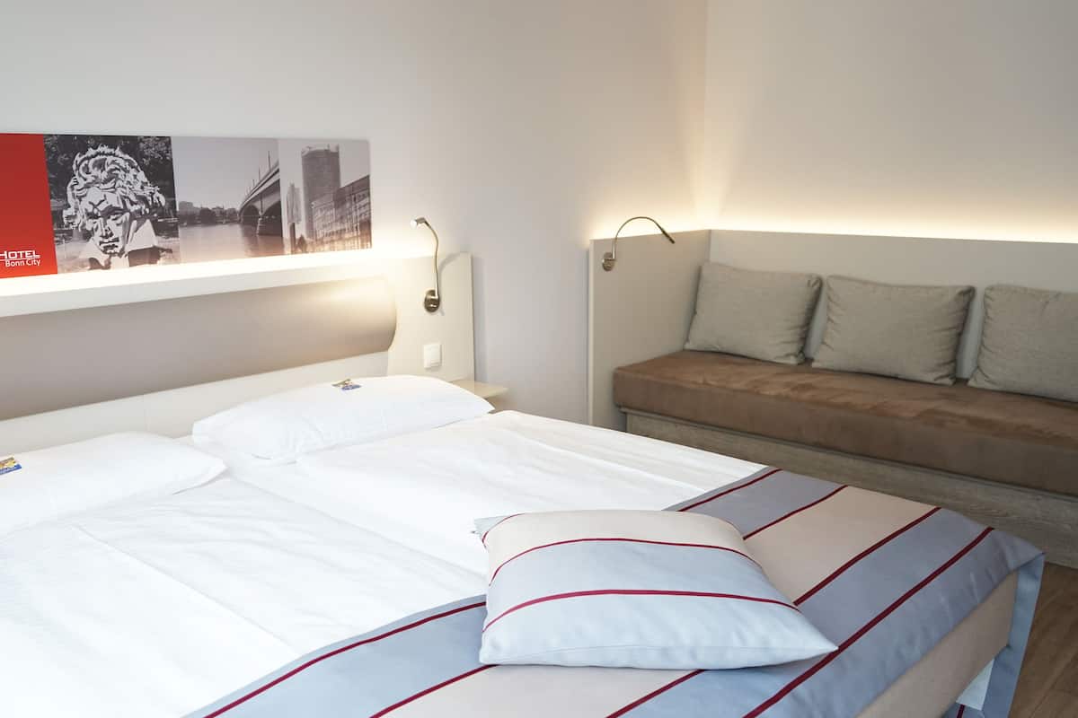 A hotel room with a bed, a sofa, a wall-mounted picture, and a nightstand.