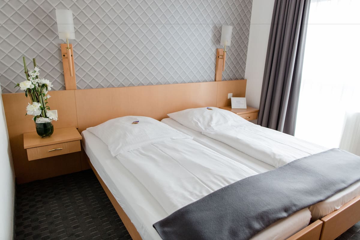A neatly made double bed with white linens, a wooden headboard, and a bedside table with a vase of flowers.