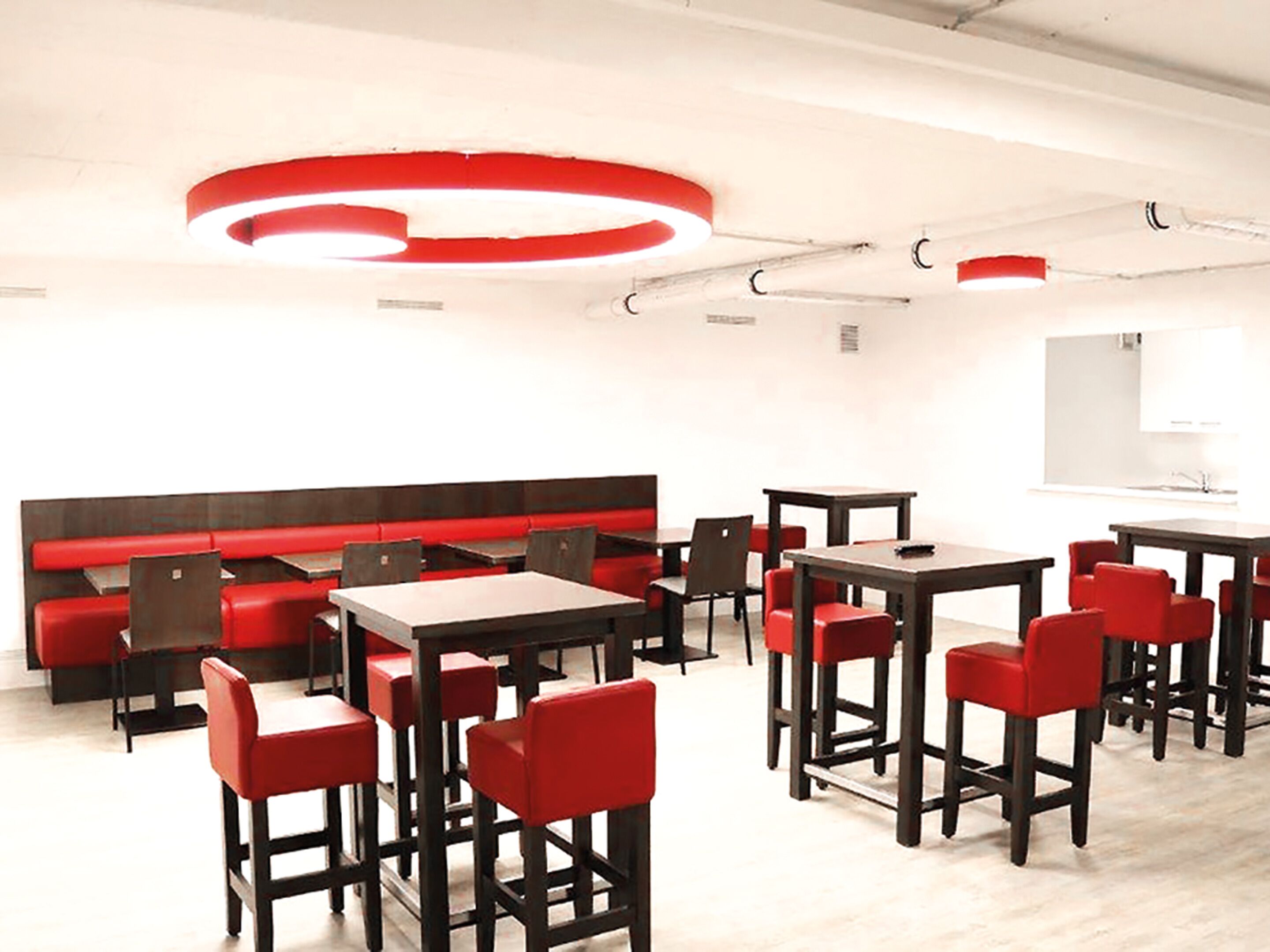 Een moderne eethoek met rood en zwart meubilair, een ronde lamp op het plafond en een witte muur met een raam.