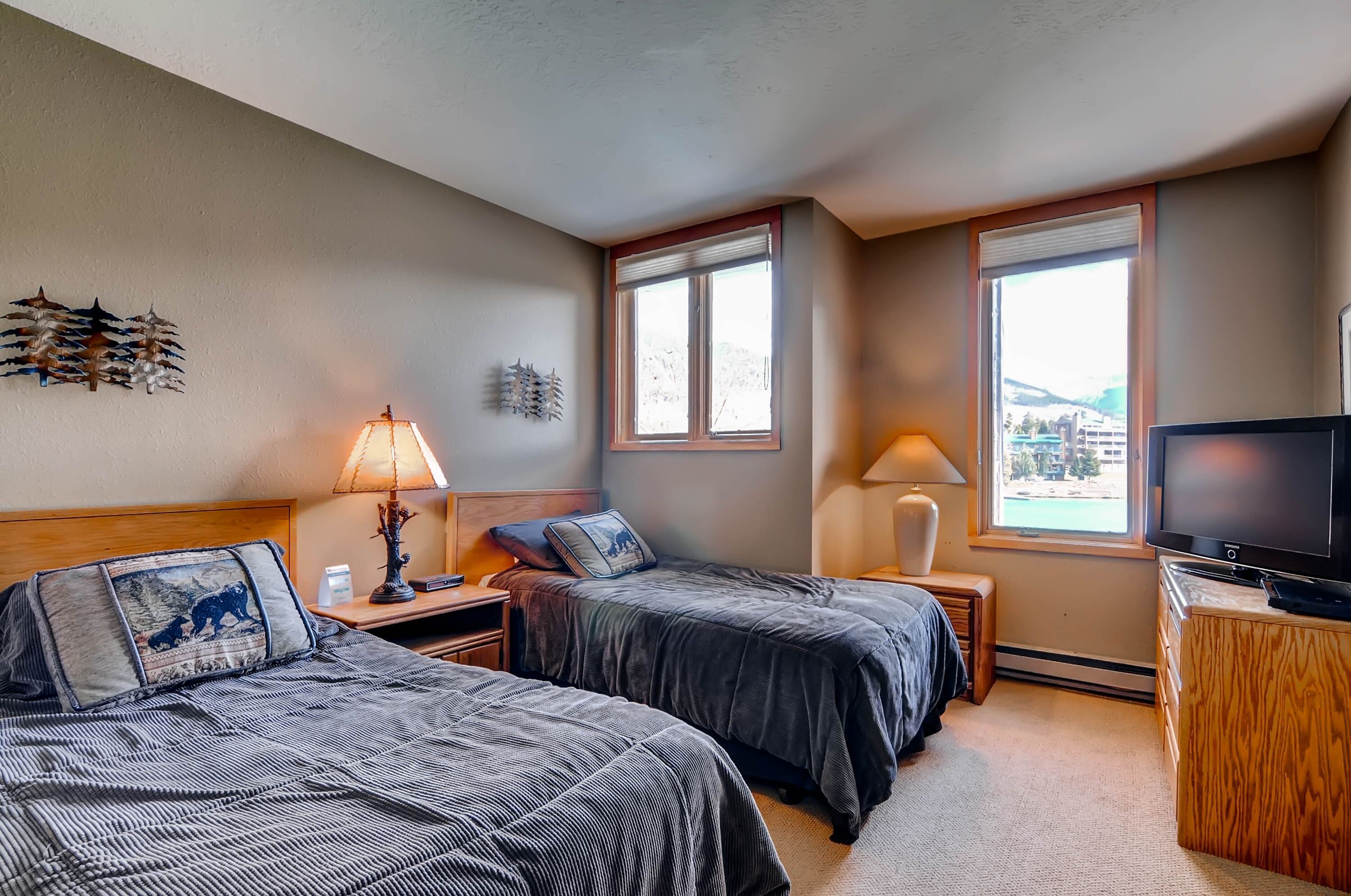 A hotel room with two beds, a TV, and two windows.