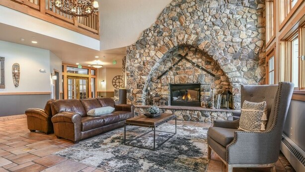 A spacious living room with a stone fireplace, leather sofas, and a chandelier.