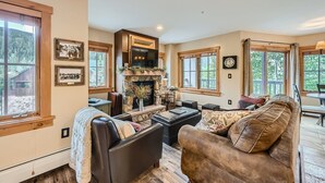 A cozy living room with a stone fireplace, leather furniture, and large windows offering a view of the outdoors.