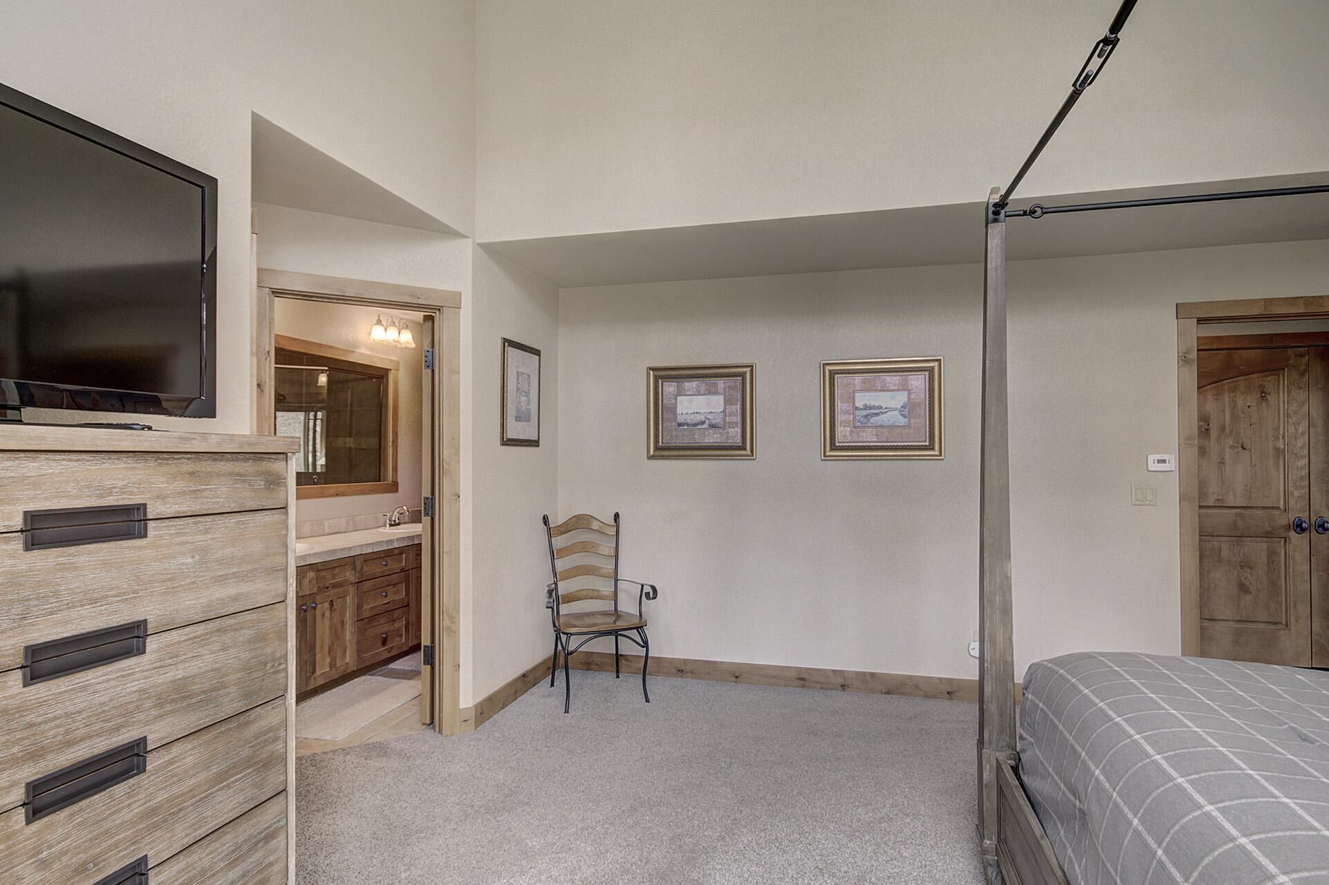 A bedroom with a bed, a TV, a wooden dresser, a chair, and framed pictures on the wall.
