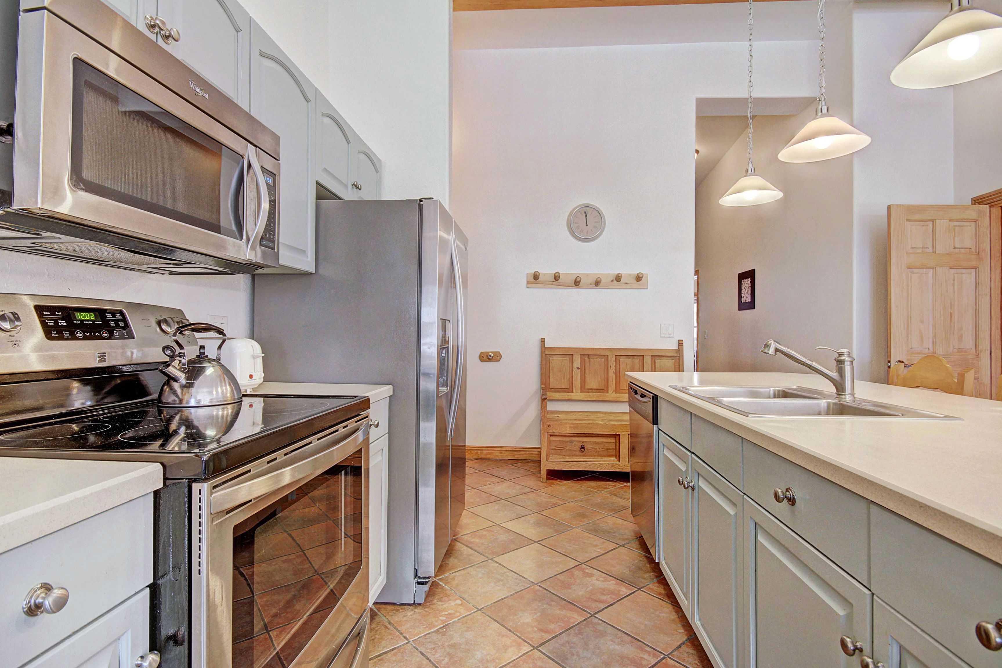 A modern kitchen with stainless steel appliances, a wooden bench, and pendant lighting.