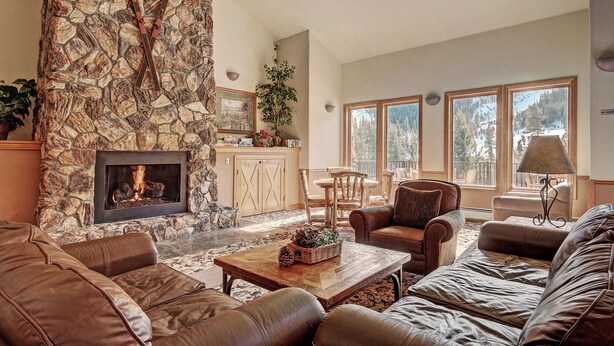 A spacious living room with a stone fireplace, leather sofas, and large windows offering a view of the outdoors.