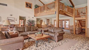 A spacious living room with leather sofas, a wooden coffee table, and a high ceiling with exposed beams.