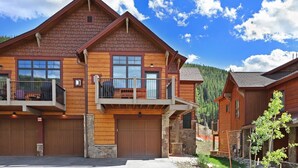 A two-story log cabin with a balcony, large windows, and a stone foundation.