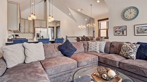 A spacious living room with a large sectional sofa, a glass coffee table, and a dining area with a chandelier.