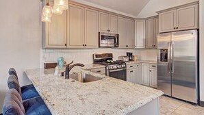 A modern kitchen with light-colored cabinets, stainless steel appliances, and a granite countertop.