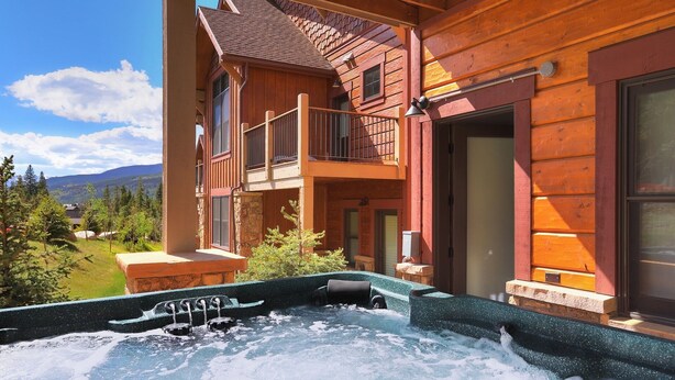 A wooden cabin with a hot tub, a balcony, and a stone fireplace.