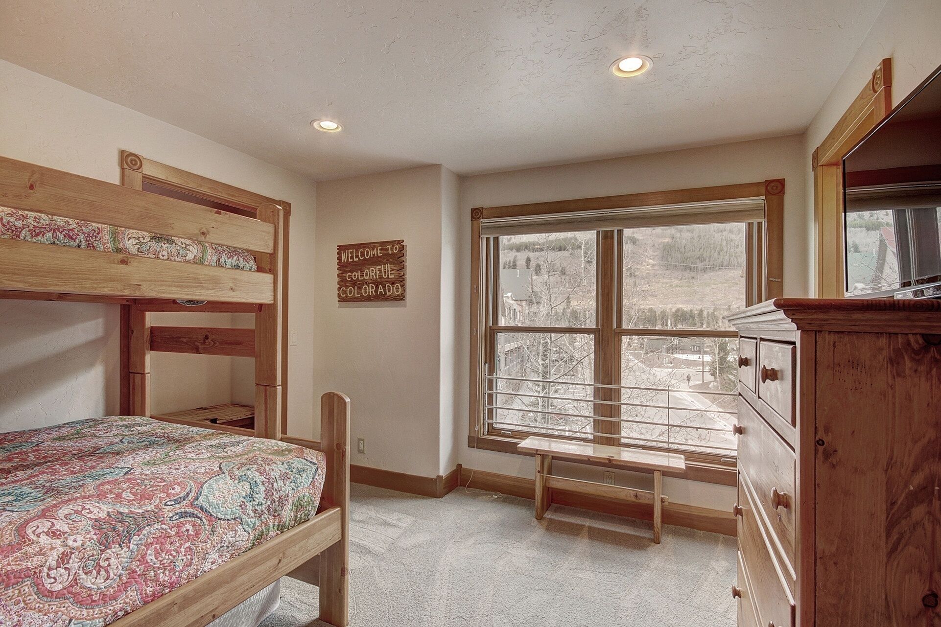 Une chambre avec des lits superposés, une grande fenêtre donnant sur un paysage enneigé, une commode en bois et un panneau d’accueil.