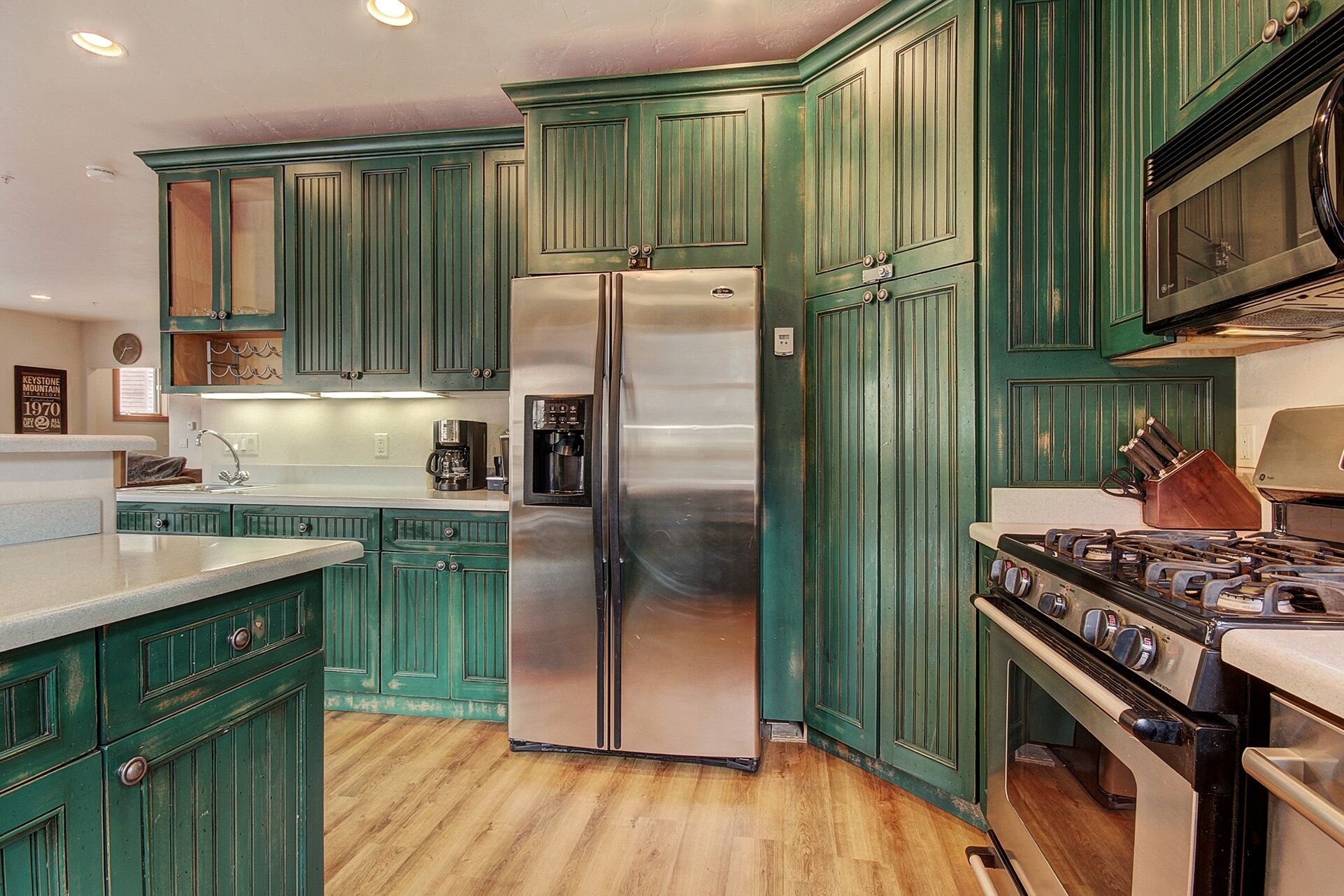 Una cocina con armarios verdes, un refrigerador de acero inoxidable, una cafetera y una estufa.